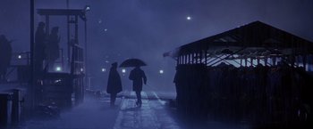 Movie still from “Crimson Tide” (1995), directed by Tony Scott – Two people walking on a train platform with an umbrella; Extreme Wide shot, Over the shoulder angle