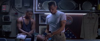 Movie still from “Crimson Tide” (1995), directed by Tony Scott – A man in a white t - shirt is looking at his cell phone; Medium shot, Low angle