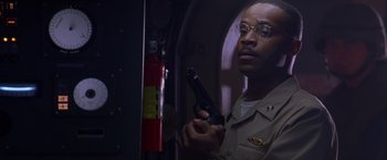 Movie still from “Crimson Tide” (1995), directed by Tony Scott – A man in uniform holding a gun in front of a fire extinguisher; Close Up shot, Low angle