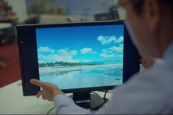 Movie still from “Cross the Line” (2020), directed by David Victori – A man pointing to a computer screen with a picture of a beach on it; Extreme Close Up shot, High angle