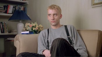 Movie still from “Croupier” (1998), directed by Mike Hodges – A man sitting on a couch in a living room; Medium shot, Low angle