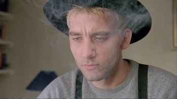 Movie still from “Croupier” (1998), directed by Mike Hodges – A person wearing a hat with smoke coming out of it; Close Up shot, Low angle