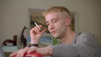 Movie still from “Croupier” (1998), directed by Mike Hodges – A man with blonde hair is smoking a cigarette; Close Up shot, Low angle