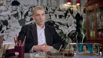 Movie still from “Croupier” (1998), directed by Mike Hodges – A man sitting at a table in front of a painting; Medium shot, Low angle
