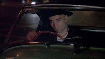 Movie still from “Croupier” (1998), directed by Mike Hodges – A man in a hat is in the drivers seat of a car; Close Up shot, High angle