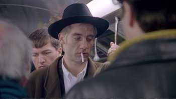 Movie still from “Croupier” (1998), directed by Mike Hodges – A man in a hat smoking a cigarette on a train; Close Up shot, Over the shoulder angle