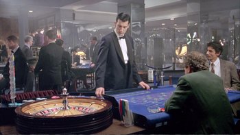 Movie still from “Croupier” (1998), directed by Mike Hodges – A man standing at a roulette table in a casino; Wide shot, High angle