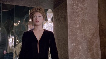 Movie still from “Croupier” (1998), directed by Mike Hodges – A woman in a black dress standing next to a pillar; Medium shot, Over the shoulder angle