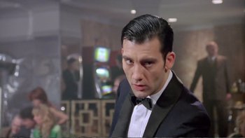 Movie still from “Croupier” (1998), directed by Mike Hodges – A man in a suit and bow tie looking to his left; Close Up shot, Low angle