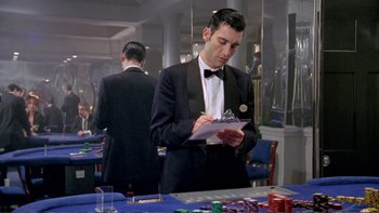 Movie still from “Croupier” (1998), directed by Mike Hodges – A man in a tuxedo writing on a piece of paper; Medium shot, High angle