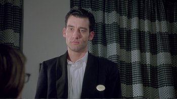 Movie still from “Croupier” (1998), directed by Mike Hodges – A man wearing a suit and a white shirt is posing for a picture; Close Up shot, Low angle