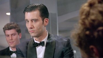 Movie still from “Croupier” (1998), directed by Mike Hodges – A man in a suit and bow tie looking into a mirror; Close Up shot, Over the shoulder angle