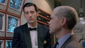 Movie still from “Croupier” (1998), directed by Mike Hodges – A man in a suit and tie looking at another man in a suit and tie; Medium shot, Over the shoulder angle