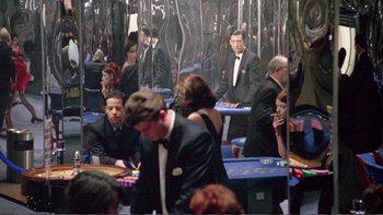 Movie still from “Croupier” (1998), directed by Mike Hodges – A group of people sitting at tables in front of a mirror; Wide shot, High angle