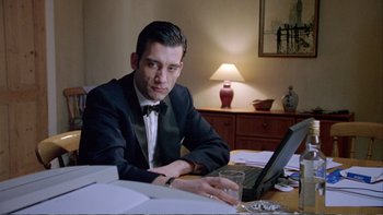 Movie still from “Croupier” (1998), directed by Mike Hodges – A man sitting at a table using a laptop computer; Medium shot, Low angle