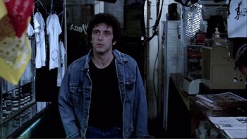 Movie still from “Cruising” (1980), directed by William Friedkin – A man standing in a dark room with his hands in his pockets; Medium shot, Low angle