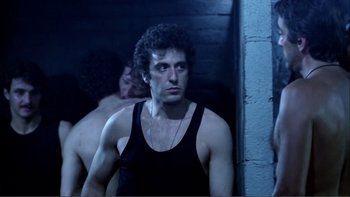 Movie still from “Cruising” (1980), directed by William Friedkin – A man in a black tank top is looking at the camera; Medium shot, Low angle