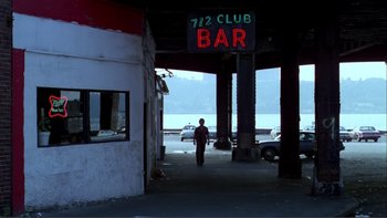 Movie still from “Cruising” (1980), directed by William Friedkin – A man walking in front of a building with a sign on it's side; Wide shot, Low angle