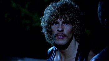 Movie still from “Cruising” (1980), directed by William Friedkin – A person wearing a wig; Close Up shot, Over the shoulder angle