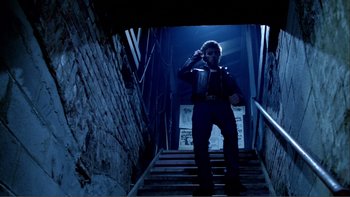 Movie still from “Cruising” (1980), directed by William Friedkin – A man standing on some stairs in the dark; Wide shot, Low angle