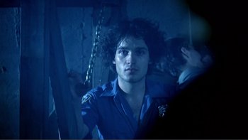 Movie still from “Cruising” (1980), directed by William Friedkin – A man with a beard is standing next to a wall; Close Up shot, Low angle