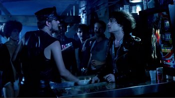 Movie still from “Cruising” (1980), directed by William Friedkin – A group of people standing around a bar; Medium shot, Over the shoulder angle