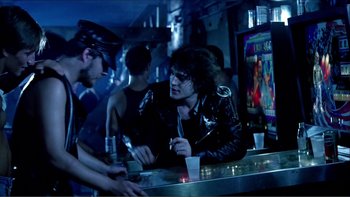Movie still from “Cruising” (1980), directed by William Friedkin – A group of young men sitting at a bar; Medium shot, Over the shoulder angle