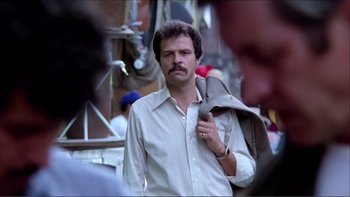 Movie still from “Cruising” (1980), directed by William Friedkin – A man with a beard and mustache holding a jacket; Close Up shot, Low angle