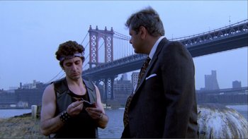 Movie still from “Cruising” (1980), directed by William Friedkin – A man and a woman standing next to each other looking at a cell phone; Medium shot, Over the shoulder angle