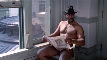 Movie still from “Cruising” (1980), directed by William Friedkin – A man sitting on a chair reading a newspaper; Medium shot, Low angle