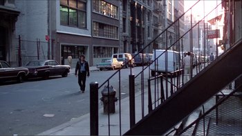 Movie still from “Cruising” (1980), directed by William Friedkin – A man walking down a street near a fire hydrant; Wide shot, Over the shoulder angle