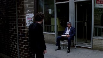 Movie still from “Cruising” (1980), directed by William Friedkin – A man sitting on a chair in front of another man; Wide shot, Over the shoulder angle