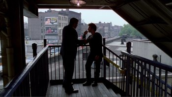 Movie still from “Cruising” (1980), directed by William Friedkin – Two men standing next to each other on a balcony; Wide shot, Over the shoulder angle