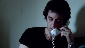 Movie still from “Cruising” (1980), directed by William Friedkin – A man is talking on a phone while sitting down; Close Up shot, Low angle