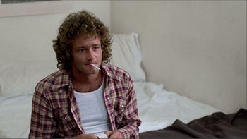 Movie still from “Cruising” (1980), directed by William Friedkin – A man sitting on a bed smoking a cigarette; Medium shot, Over the shoulder angle