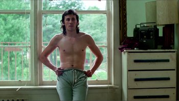 Movie still from “Cruising” (1980), directed by William Friedkin – A man standing in front of a window with his hands on his hips; Medium shot, Low angle