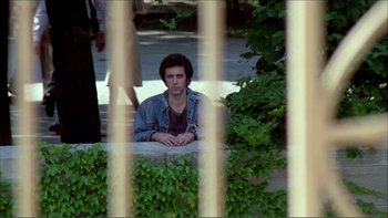 Movie still from “Cruising” (1980), directed by William Friedkin – A man sitting on top of a wall near bushes; Medium shot, High angle