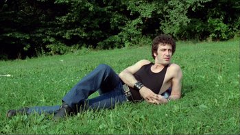 Movie still from “Cruising” (1980), directed by William Friedkin – A man laying in the grass with a guitar; Medium shot, Low angle