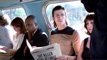 Movie still from “Cruising” (1980), directed by William Friedkin – A man sitting on a bus reading a newspaper; Medium shot, Over the shoulder angle