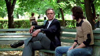 Movie still from “Cruising” (1980), directed by William Friedkin – A man sitting on top of a wooden park bench; Medium shot, Low angle