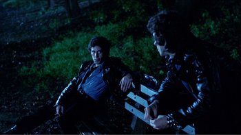 Movie still from “Cruising” (1980), directed by William Friedkin – Two men sitting on a bench in the dark; Medium shot, Over the shoulder angle