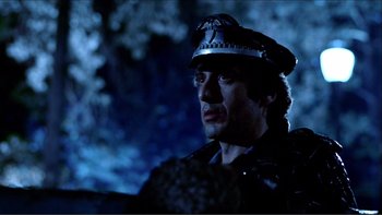 Movie still from “Cruising” (1980), directed by William Friedkin – A man wearing a police hat in the dark with trees in the background; Close Up shot, Low angle