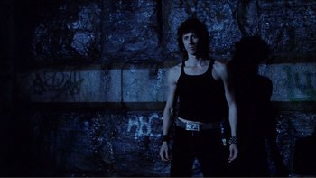 Movie still from “Cruising” (1980), directed by William Friedkin – A man standing in front of a stone wall; Medium shot, Low angle