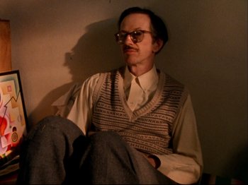 Movie still from “Crumb” (1994), directed by Terry Zwigoff – A man sitting on the ground wearing glasses and a sweater vest; Medium shot, Low angle