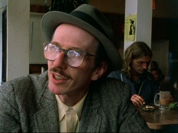 Movie still from “Crumb” (1994), directed by Terry Zwigoff – A man in a hat and glasses sitting at a table; Close Up shot, Low angle