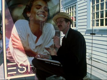 Movie still from “Crumb” (1994), directed by Terry Zwigoff – A man sitting in front of an advertisement; Medium shot, Low angle