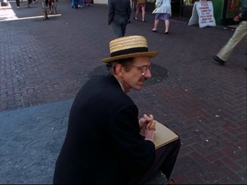 Movie still from “Crumb” (1994), directed by Terry Zwigoff – An older man wearing a straw hat sitting on the ground; Medium shot, High angle