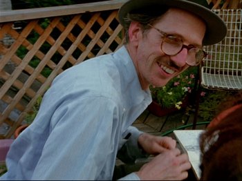 A man wearing glasses and a hat is smiling for the camera