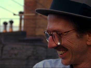Movie still from “Crumb” (1994), directed by Terry Zwigoff – A person wearing glasses and a hat; Close Up shot, Over the shoulder angle