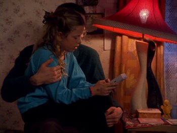Movie still from “Crumb” (1994), directed by Terry Zwigoff – A young girl sitting next to a man holding a phone; Medium shot, High angle